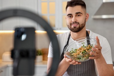 Photo of Food blogger cooking while recording video with smartphone and ring lamp in kitchen