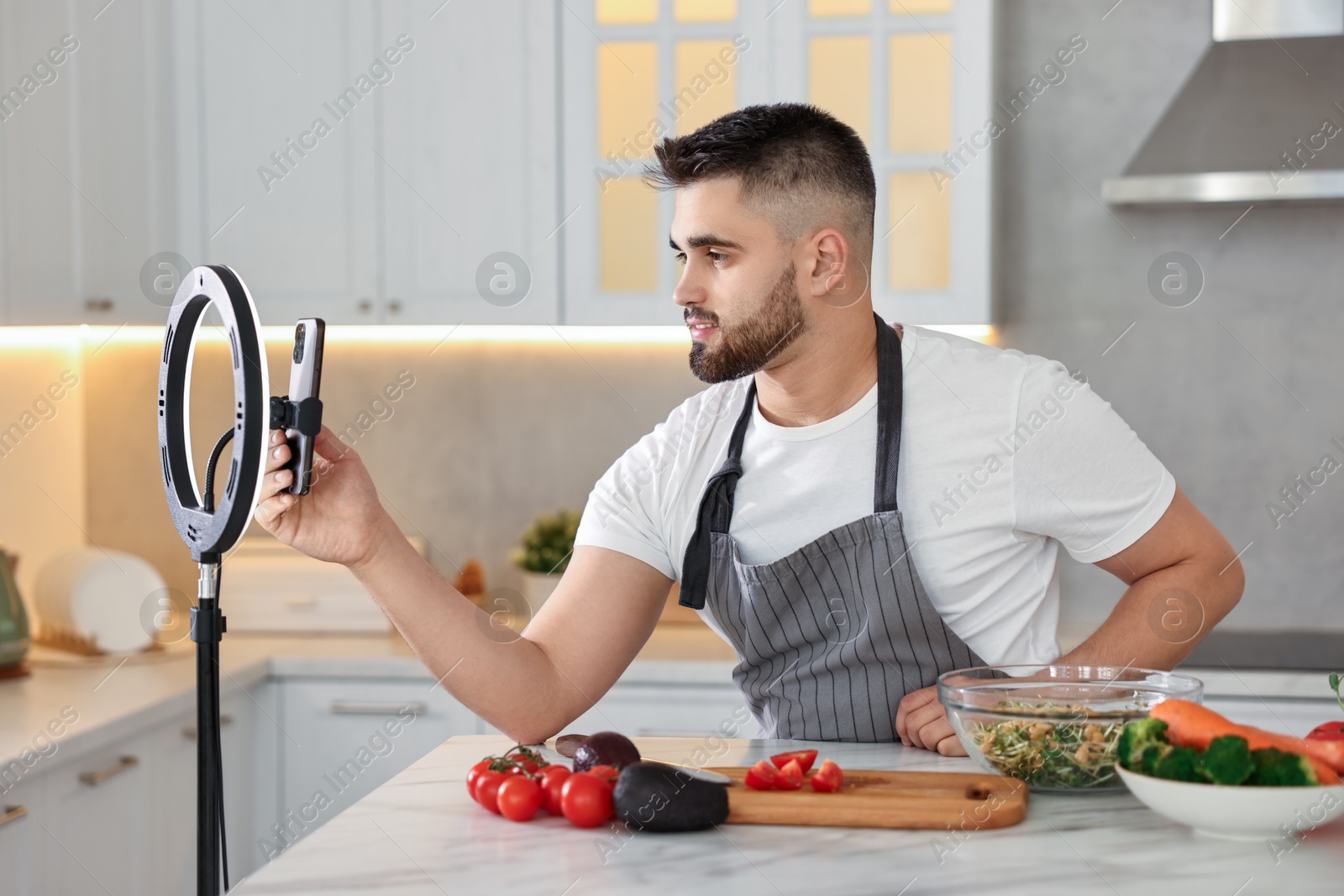 Photo of Food blogger cooking while recording video with smartphone and ring lamp in kitchen