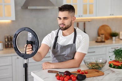 Food blogger cooking while recording video with smartphone and ring lamp in kitchen