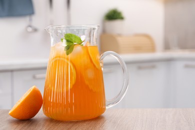 Photo of Freshly made lemonade in jug, mint and orange on wooden table in kitchen, space for text