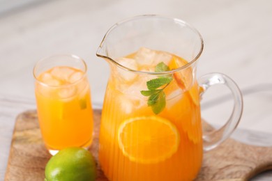 Photo of Tasty lemonade with orange in jug, glass and lime on table