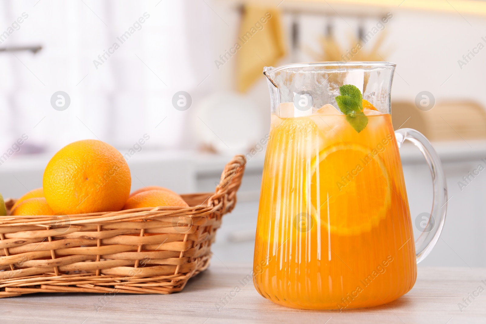 Photo of Freshly made lemonade in jug and oranges on wooden table in kitchen