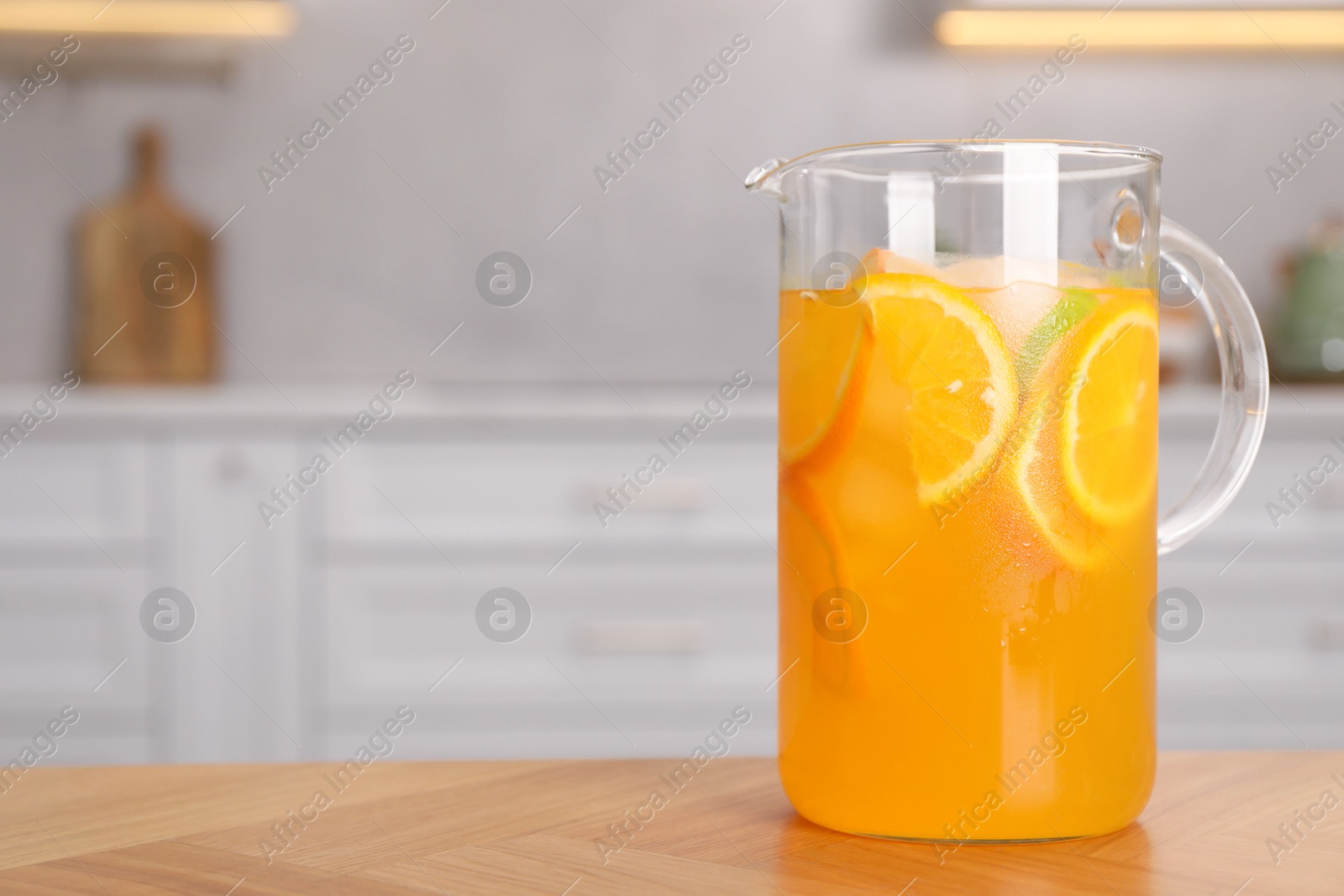 Photo of Freshly made lemonade in jug on wooden table in kitchen, space for text