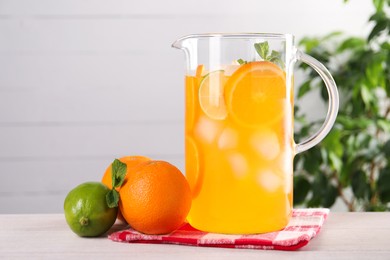 Freshly made lemonade in jug and citrus fruits on light wooden table