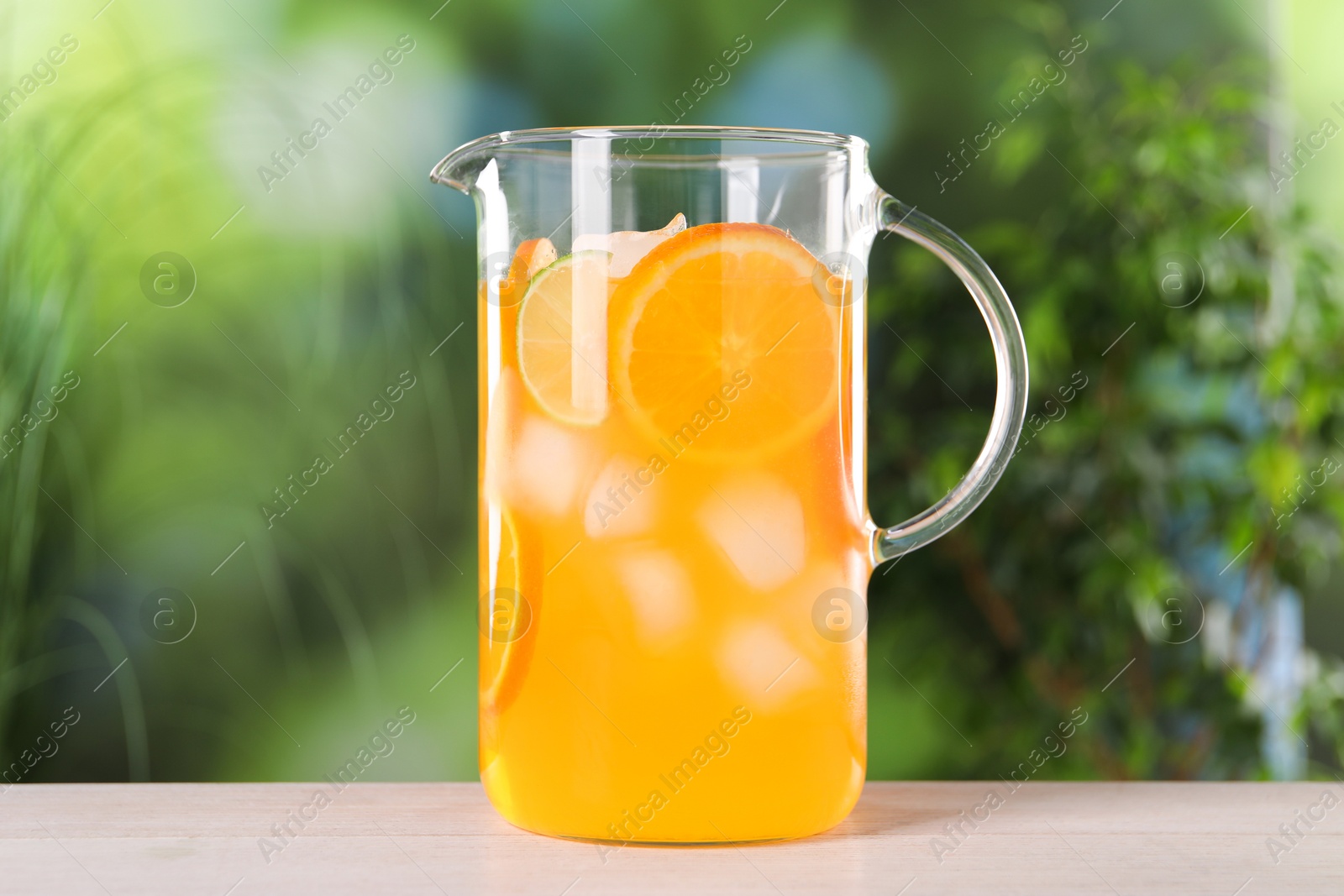 Photo of Freshly made lemonade in jug on light wooden table outdoors