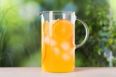 Photo of Freshly made lemonade in jug on light wooden table outdoors