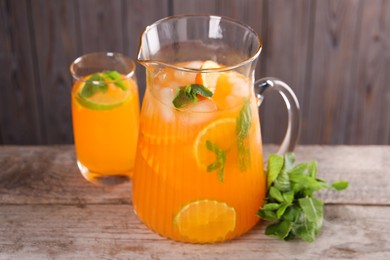 Photo of Freshly made lemonade in jug, glass and mint on wooden table