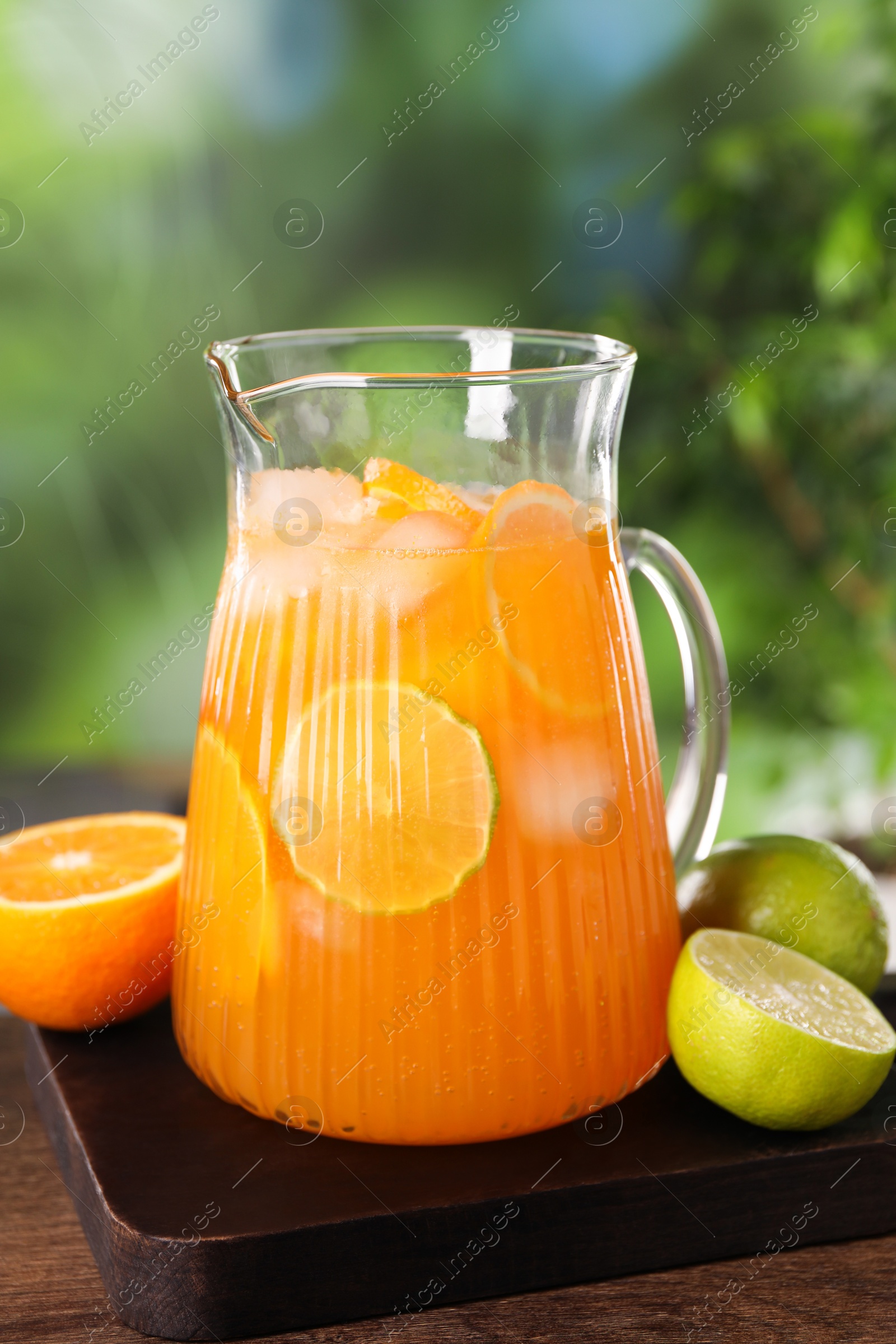 Photo of Freshly made lemonade in jug and citrus fruits on wooden table outdoors