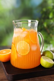 Photo of Freshly made lemonade in jug and citrus fruits on wooden table outdoors