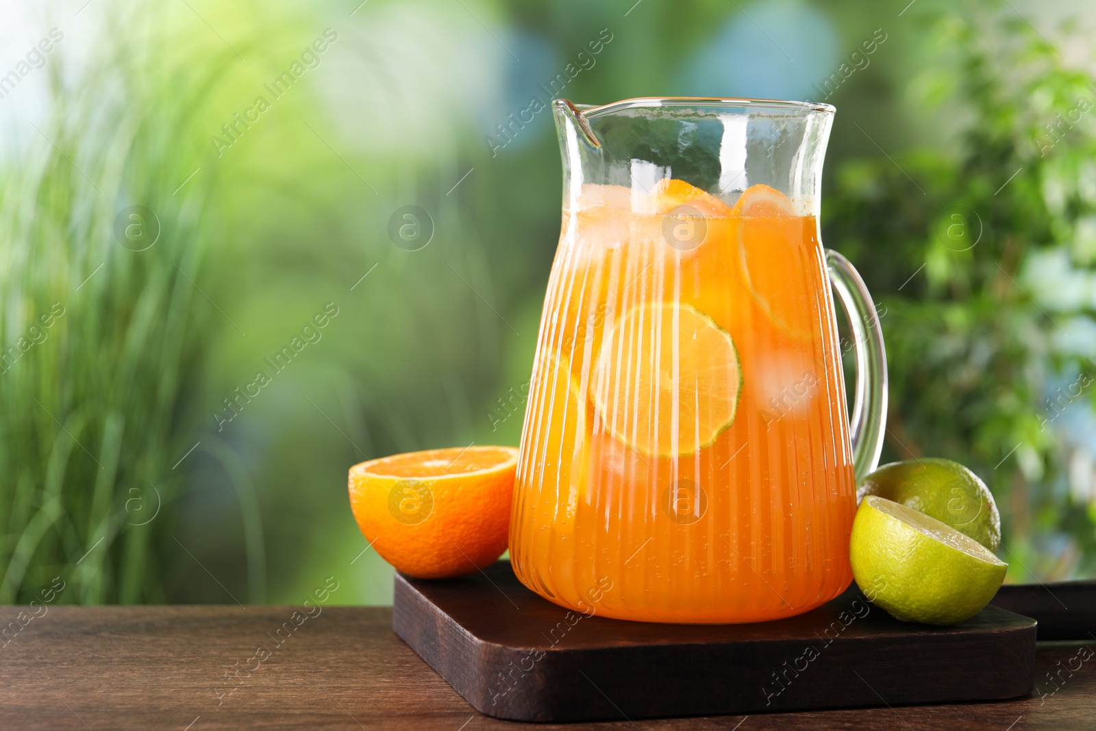 Photo of Freshly made lemonade in jug and citrus fruits on wooden table outdoors, space for text