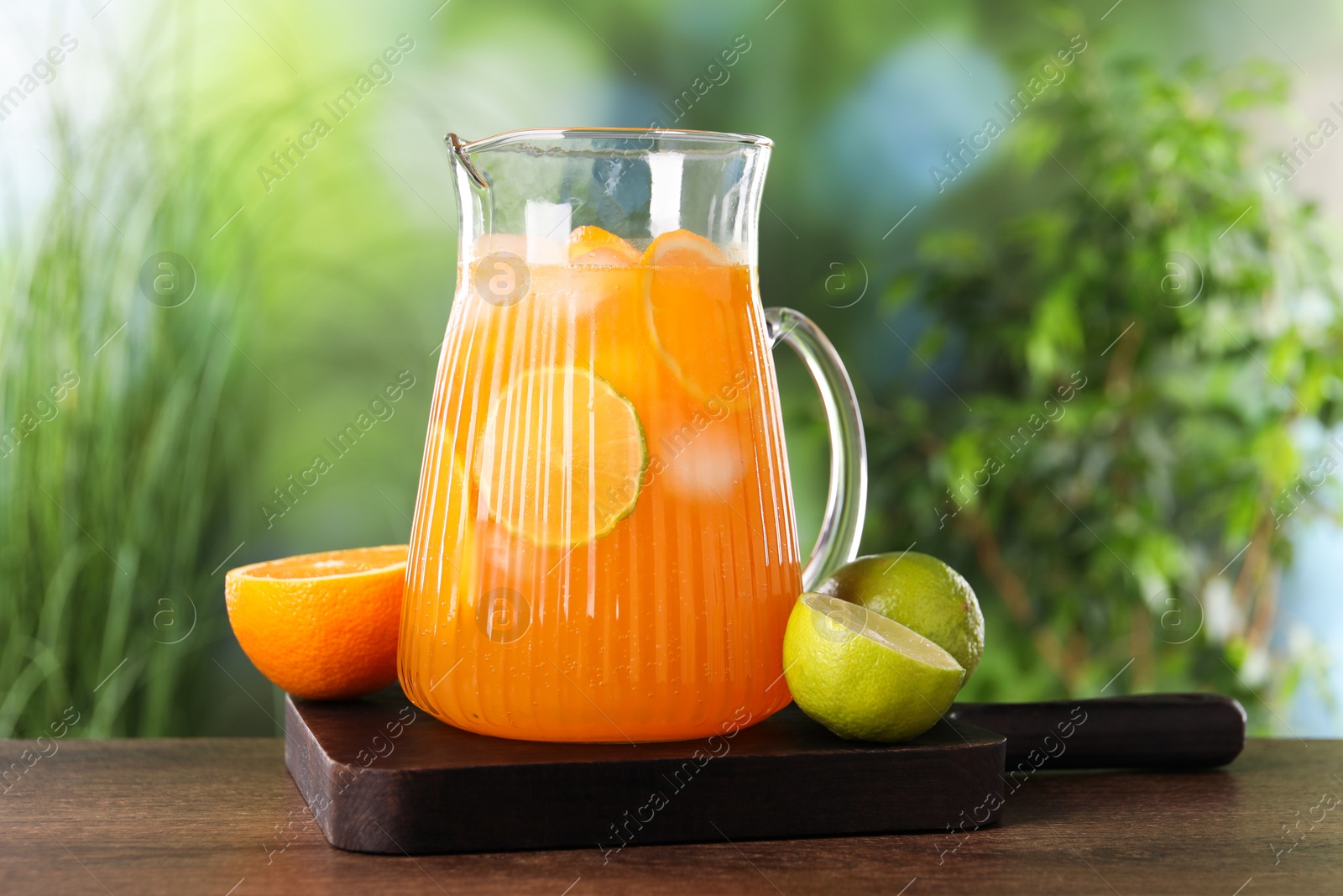 Photo of Freshly made lemonade in jug and citrus fruits on wooden table outdoors