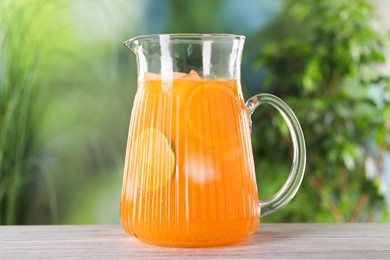 Photo of Freshly made lemonade in jug on wooden table outdoors