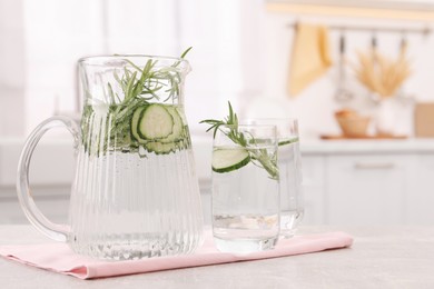 Refreshing cucumber water with rosemary on table in kitchen. Space for text