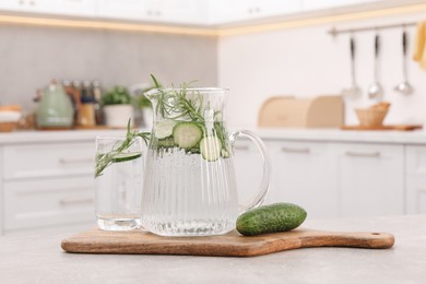 Photo of Refreshing cucumber water with rosemary and vegetable on table in kitchen