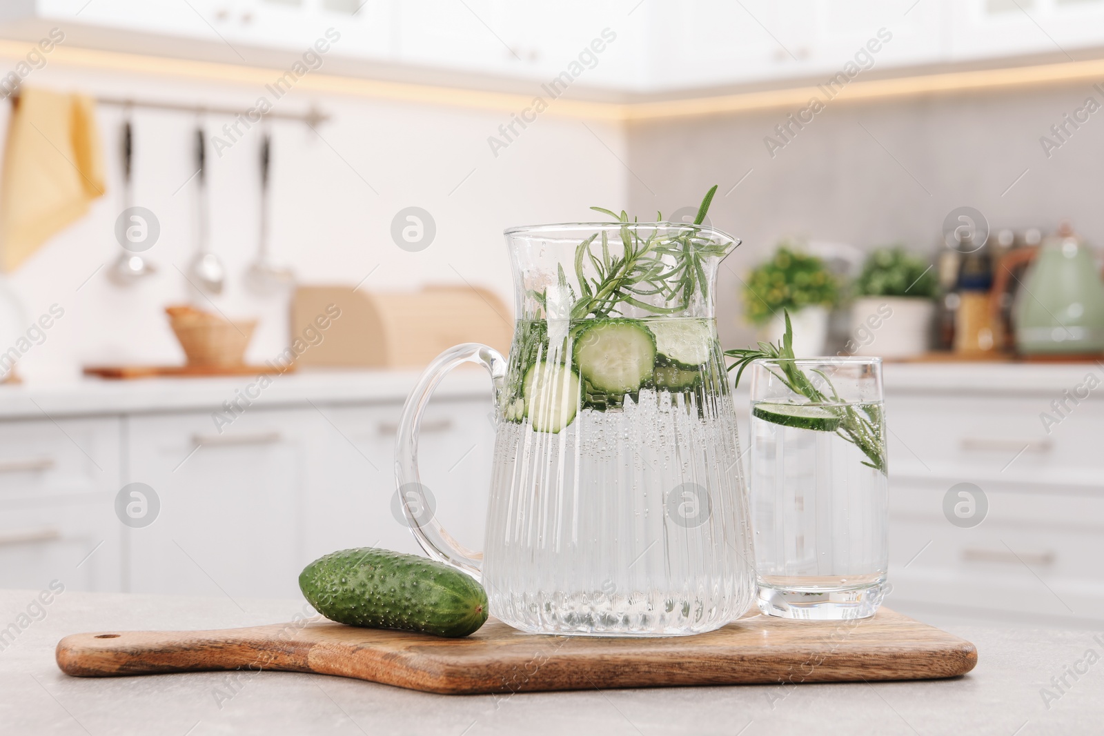 Photo of Refreshing cucumber water with rosemary and vegetable on table in kitchen