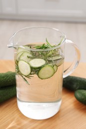 Refreshing cucumber water with rosemary in jug and vegetable on wooden table, closeup