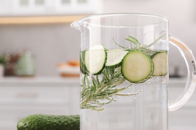 Refreshing cucumber water with rosemary in jug and vegetable on blurred background, closeup