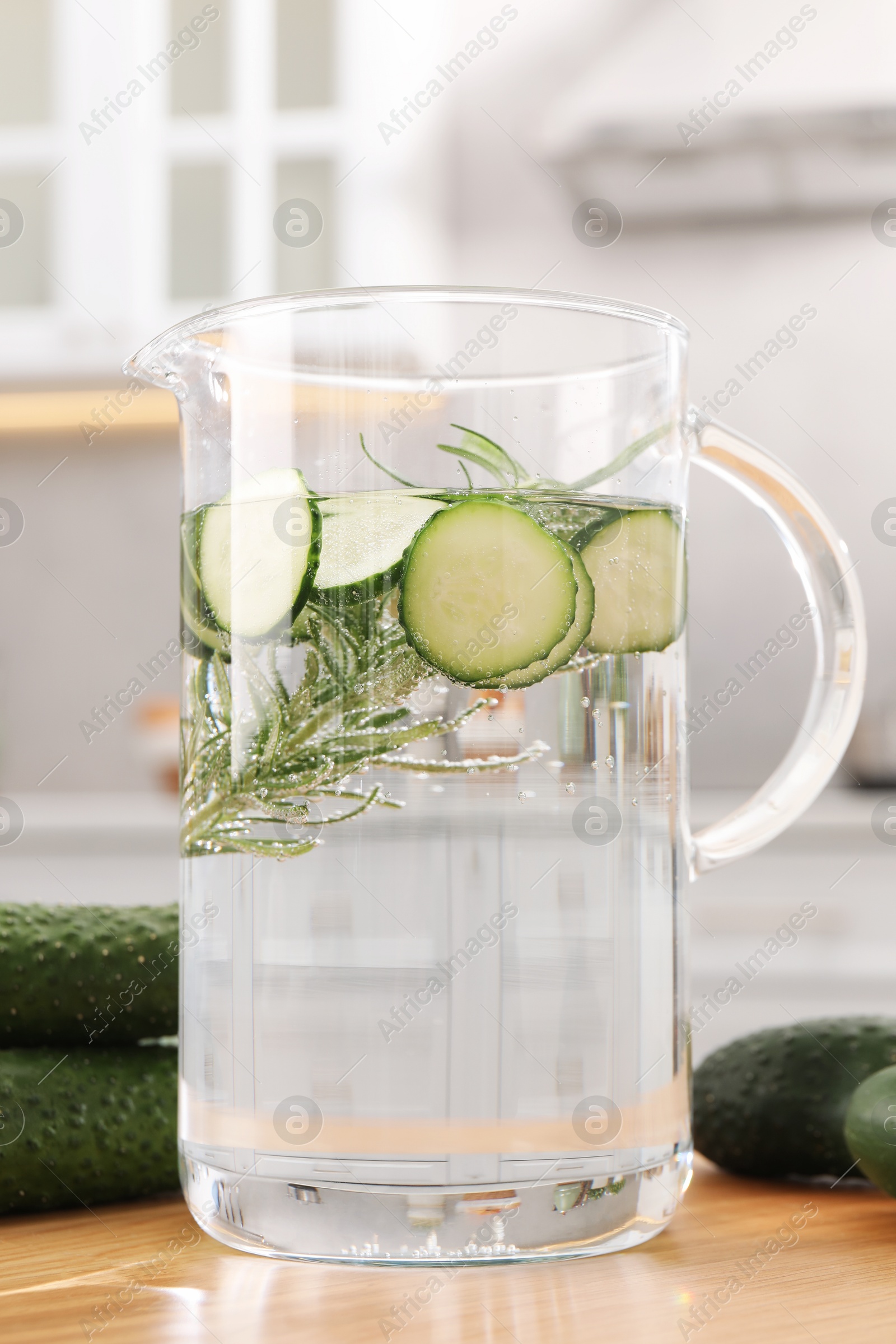 Photo of Refreshing cucumber water with rosemary in jug and vegetable on wooden table, closeup