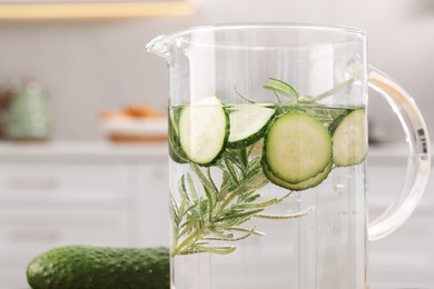 Photo of Refreshing cucumber water with rosemary in jug and vegetable on blurred background, closeup