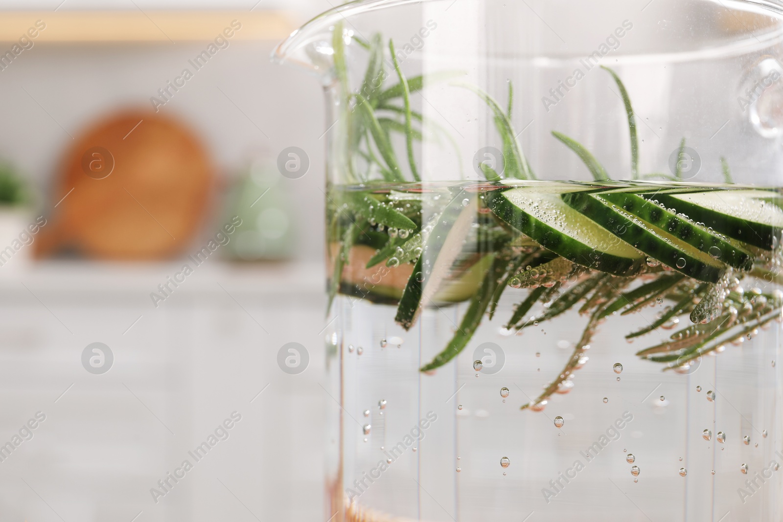 Photo of Refreshing cucumber water with rosemary in jug on blurred background, closeup. Space for text