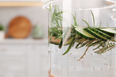 Refreshing cucumber water with rosemary in jug on blurred background, closeup. Space for text