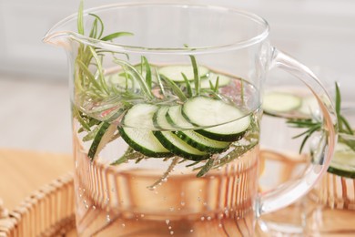 Photo of Refreshing cucumber water with rosemary in jug on blurred background, closeup