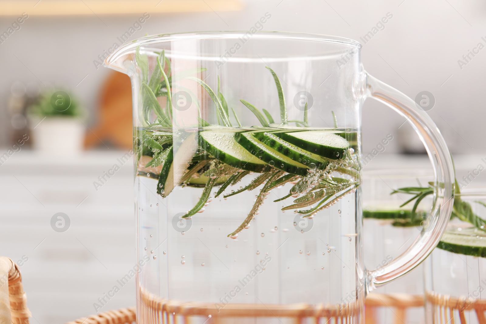 Photo of Refreshing cucumber water with rosemary in jug on blurred background, closeup