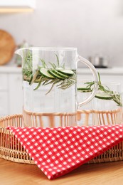 Refreshing cucumber water with rosemary in jug and glass on wooden table