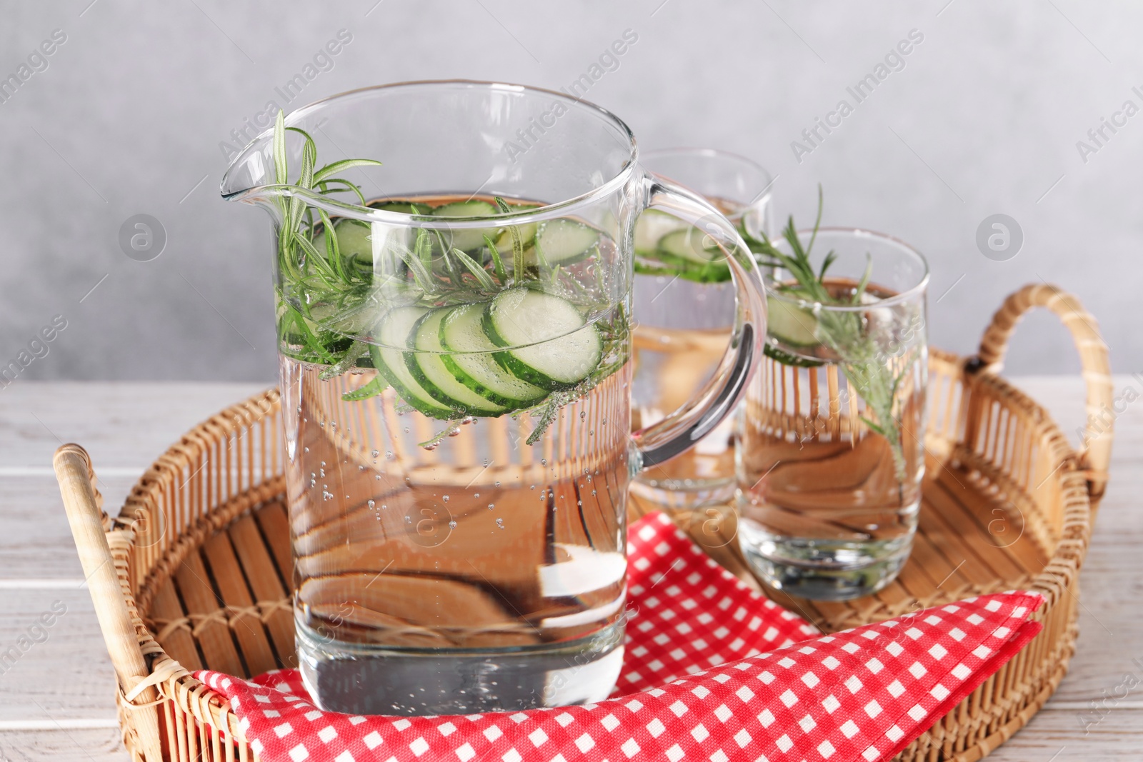 Photo of Refreshing cucumber water with rosemary in jug and glass on light wooden table