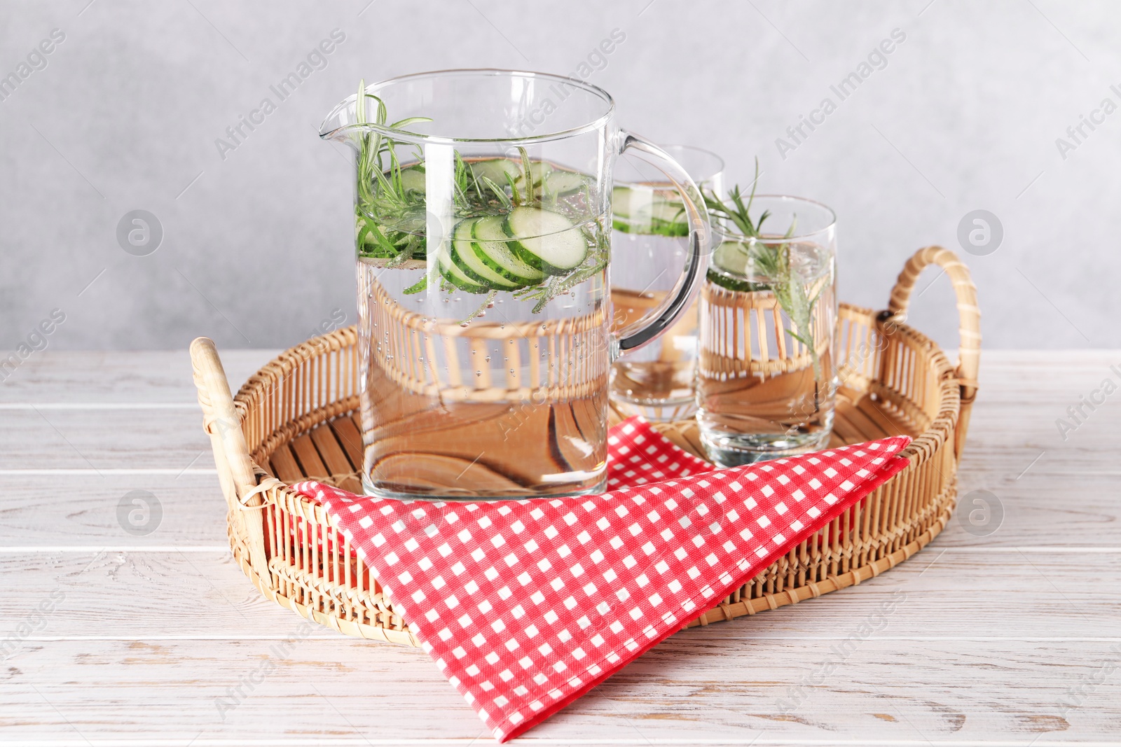 Photo of Refreshing cucumber water with rosemary in jug and glass on light wooden table