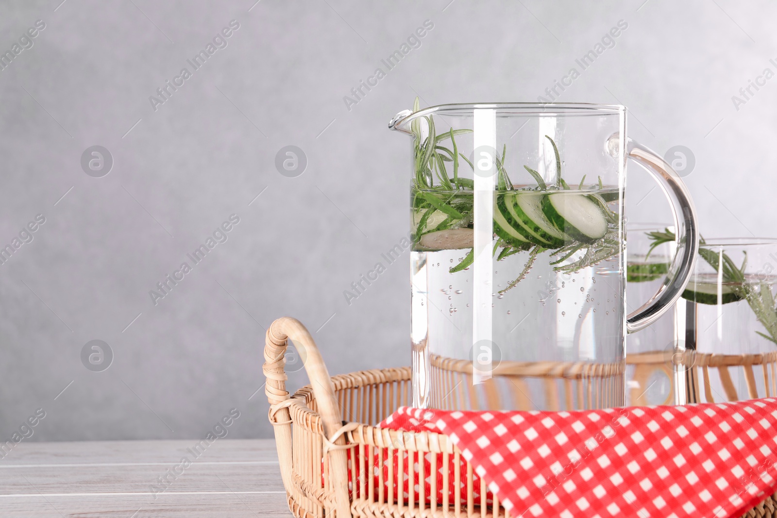 Photo of Refreshing cucumber water with rosemary in jug and glass on light wooden table. Space for text