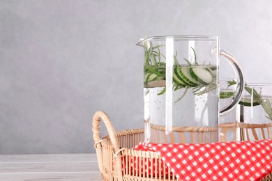 Refreshing cucumber water with rosemary in jug and glass on light wooden table. Space for text