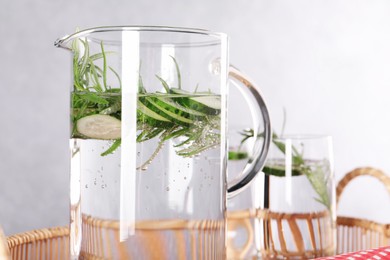 Refreshing cucumber water with rosemary in jug and glass on light grey background, closeup