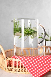 Refreshing cucumber water with rosemary in jug on light wooden table