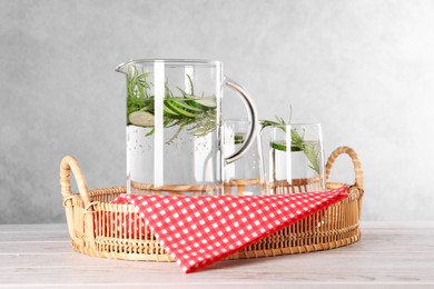 Refreshing cucumber water with rosemary in jug and glass on light wooden table