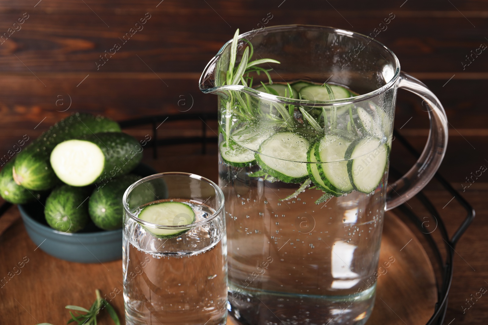 Photo of Tray with refreshing cucumber water with rosemary and vegetable on wooden table, closeup