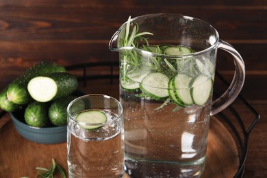 Photo of Tray with refreshing cucumber water with rosemary and vegetable on wooden table, closeup