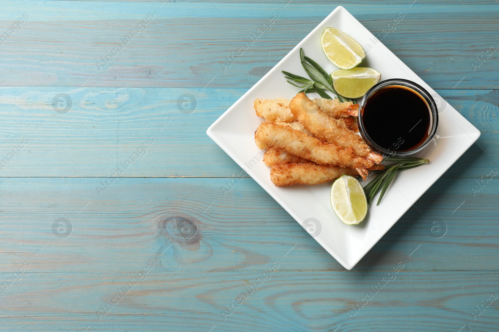 Photo of Delicious breaded fried shrimps served on light blue wooden table, top view. Space for text