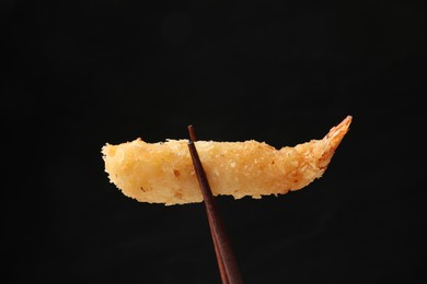 Photo of Chopsticks with delicious breaded fried shrimp on black background