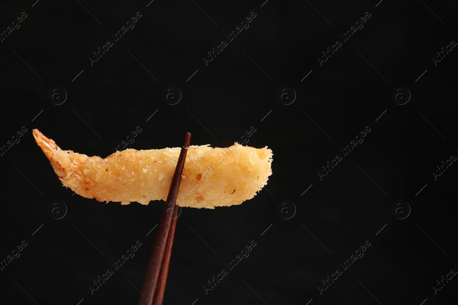 Photo of Chopsticks with delicious breaded fried shrimp on black background. Space for text