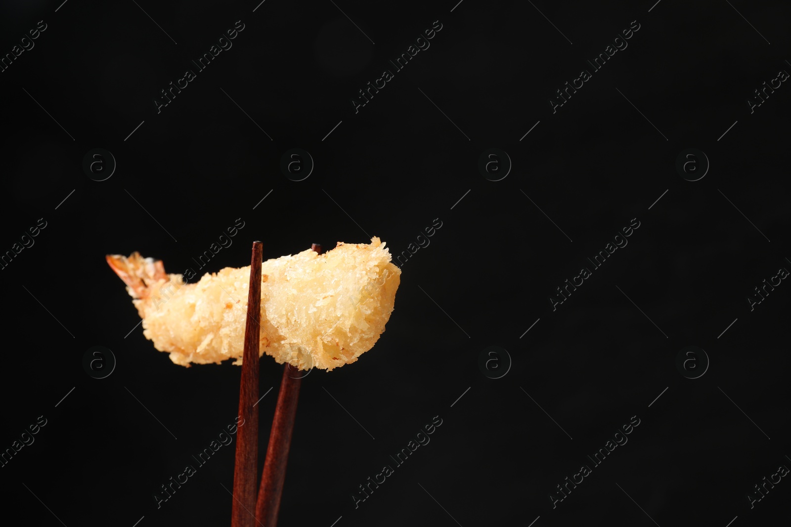 Photo of Chopsticks with delicious breaded fried shrimp on black background. Space for text