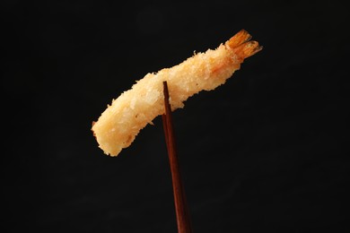 Chopsticks with delicious breaded fried shrimp on black background