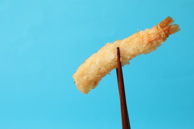 Photo of Chopsticks with delicious breaded fried shrimp on light blue background. Space for text