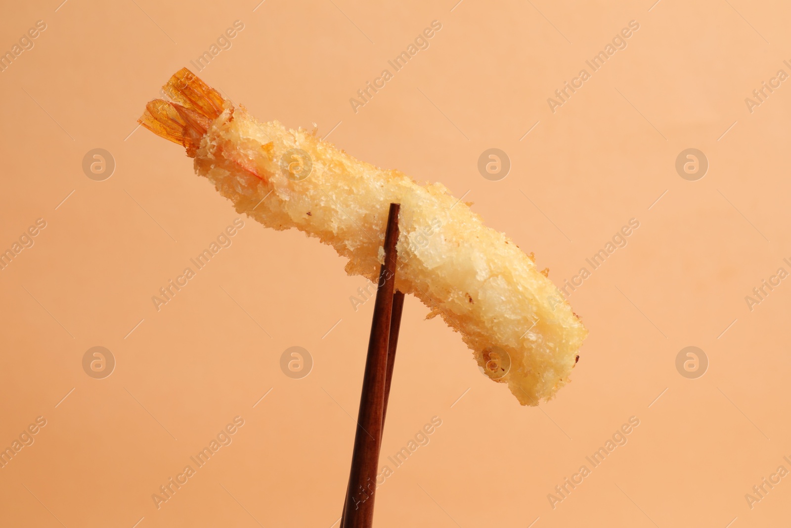 Photo of Chopsticks with delicious breaded fried shrimp on beige background