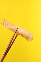 Chopsticks with delicious breaded fried shrimp on yellow background