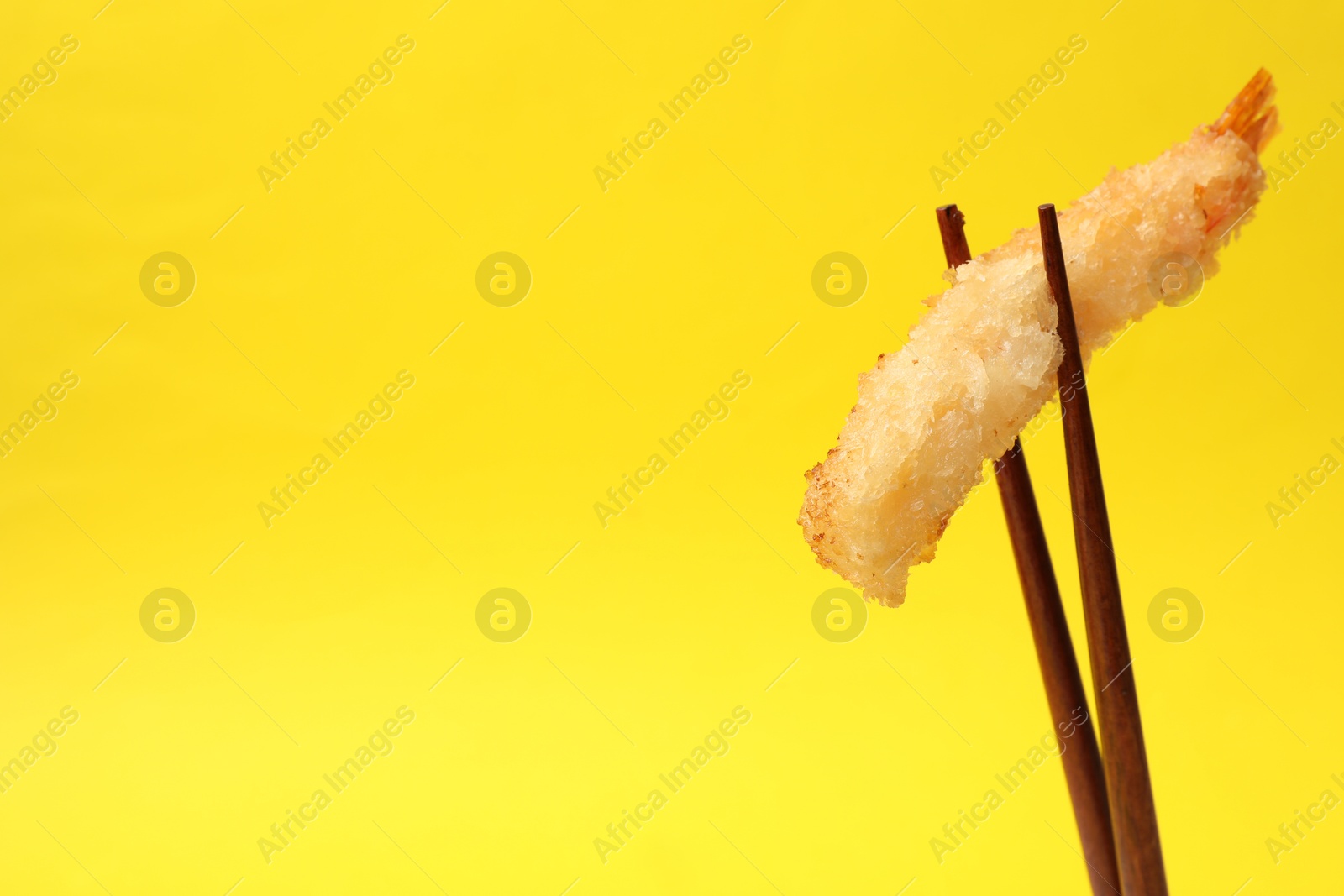 Photo of Chopsticks with delicious breaded fried shrimp on yellow background. Space for text