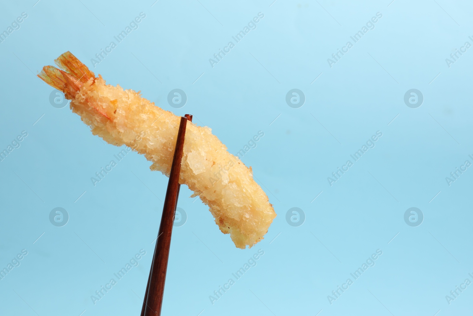 Photo of Chopsticks with delicious breaded fried shrimp on light blue background. Space for text