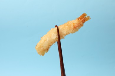 Chopsticks with delicious breaded fried shrimp on light blue background