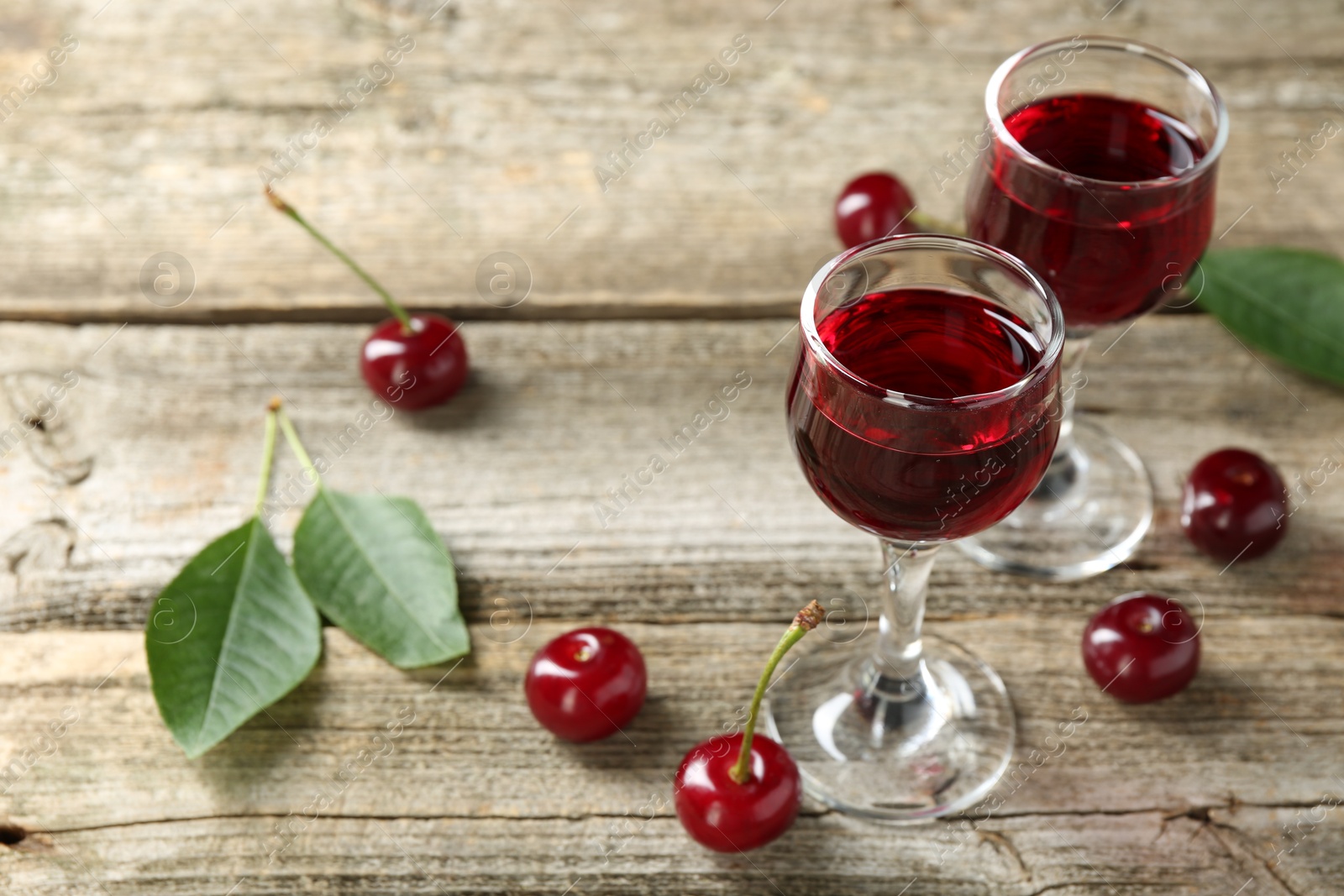 Photo of Glasses of delicious cherry liqueur and juicy berries on wooden table