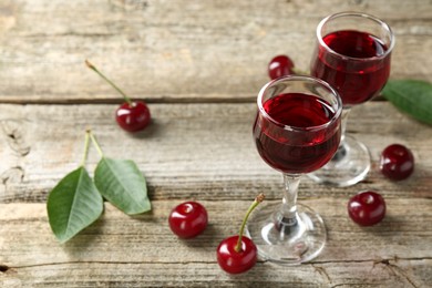Glasses of delicious cherry liqueur and juicy berries on wooden table
